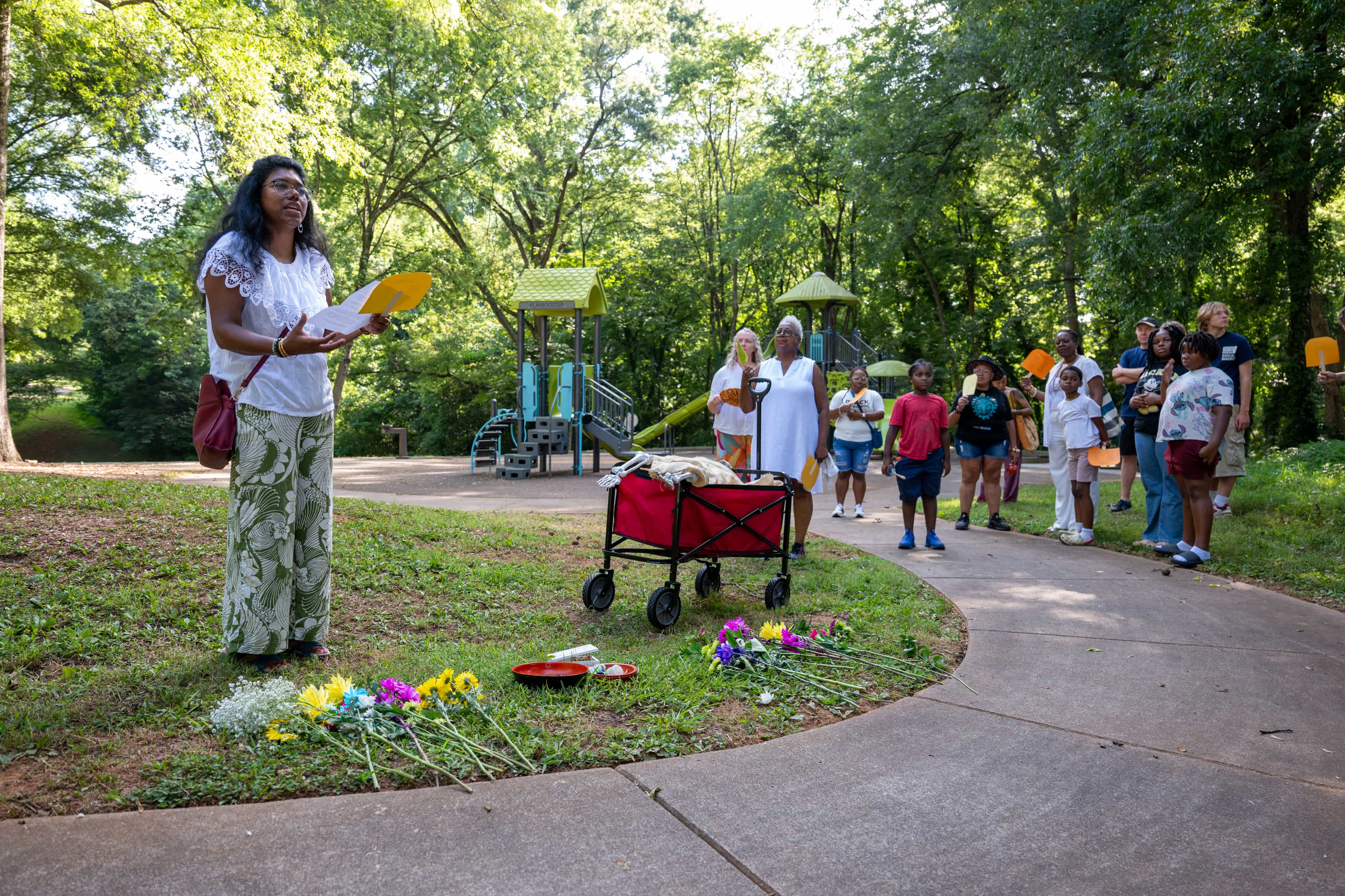 People gathered at park listening to speakder with flowers in front of them